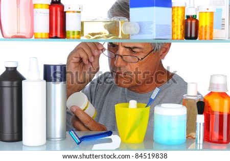 Unshaven Middle aged man reading a prescription label in front of his bathroom Medicine Cabinet. Horizontal format isolated on white.