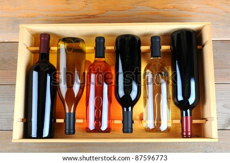 A wooden case of assorted wine bottles without labels on a wood plank winery floor. Horizontal format overhead view.