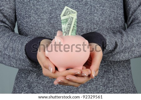 Closeup of a woman holding a piggy bank in front of her body. Bank has a dollar bill sticking in the top slot.
