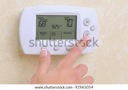 Closeup of a woman\'s hand setting the room temperature on a modern programmable thermostat.