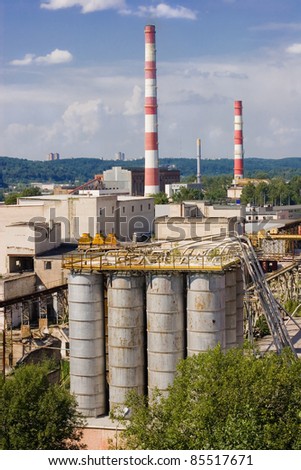 Big factory with several chimneys and cistern on a blue sky and beautiful landscape in the background.