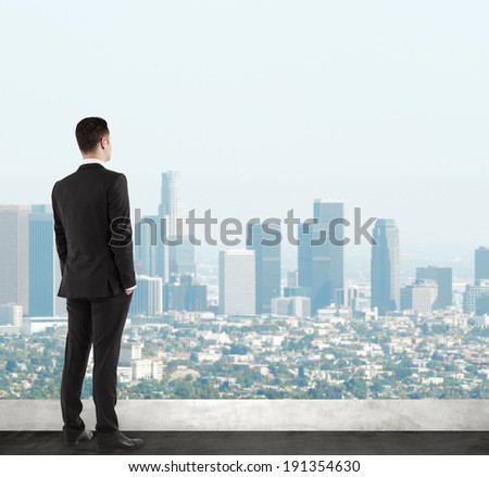 businessman in suit standing on roof and looking at city