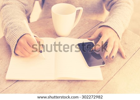 girl writes in a notebook, with cell phone and cup of coffee, vintage color effect
