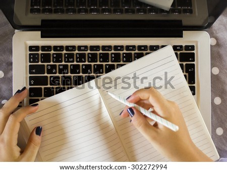 girl writes in a notebook, with laptop