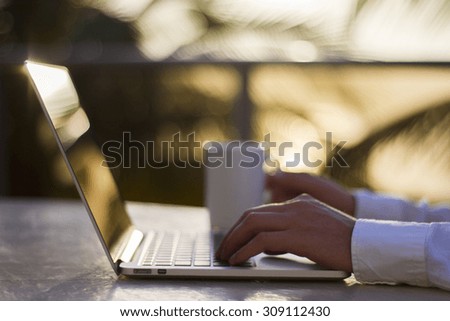 Man with laptop and cup of coffee at sunrise