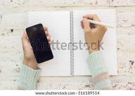 Girl hands with smartphone and blank diary with pen on a wooden table