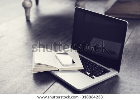 Cell phone with open book and laptop on the floor