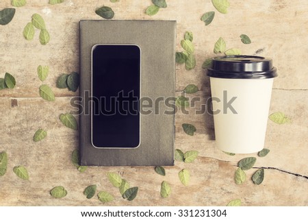 Blank smartphone on the book with cup of coffee to go on the wooden table, mock up