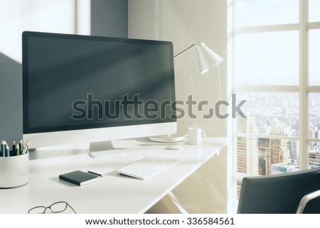 Blank computer monitor with glasses, diary and other accesories on white table in modern room