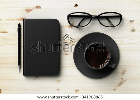 Black blank diary cover, black cup of coffee and glasses on wooden table, mock up