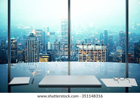 Modern office with glassy table, laptop and night megapolis city view