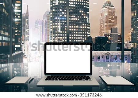Blank white laptop screen on glassy table in modern office with night megapolis city view, mock up