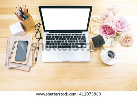 Girly office desktop with blank white laptop screen, flowers, coffee, smartphone and various office tools. Mock up