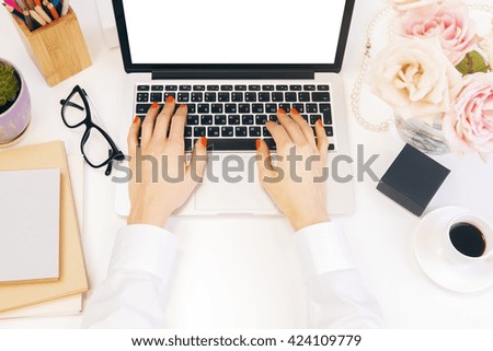 Female hands using laptop with blank white screen on designer desktop with flowers, coffee, glasses and other items. Top view, Mock up