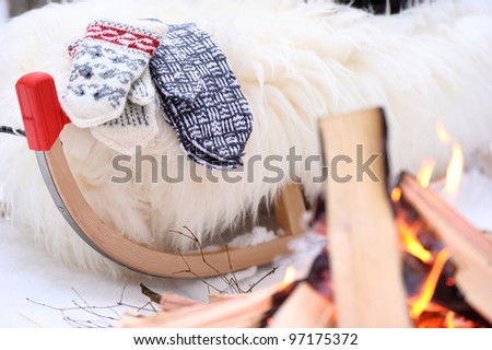 Whine rug and two pairs of mittens on sled close to bonfire on sunny winter day in forest.
