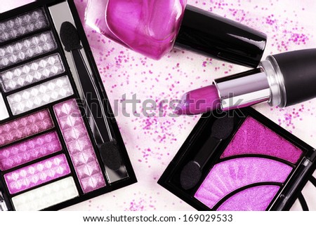 Pink eye shadow sets, lipstick and nail polish over shiny pink-white background covered with glitter