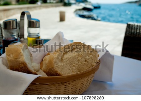 The bread and olive oil is standing on the table next to the ocean.
