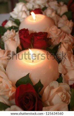 Two candles situated in a bunch of red and white roses.