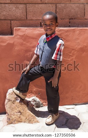 A young little boy with his foot on the rock being photographed in formal clothing.