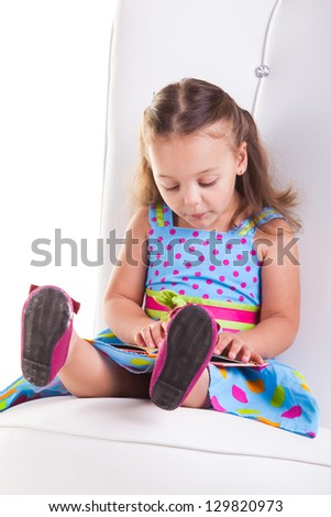 Little girl sitting on a big chair, busy with her books.