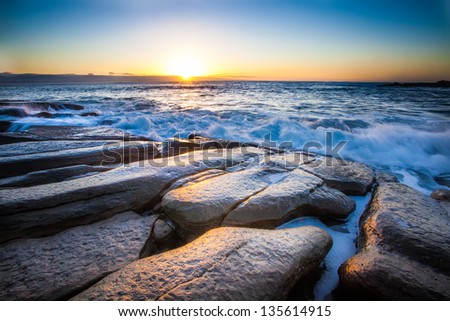 the breaking dawn over a rocky shore and lively sea