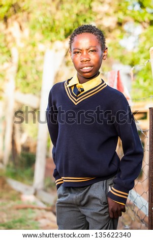 an teenage african boy readily dressed in his school clothes waiting by the fence before school starts