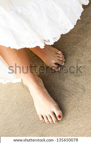 a close-up on a dress being lift up to reveal slim sandy feet with red toenails