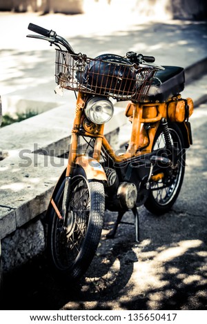 an old orange scooter with a rusty basket parked on the curb