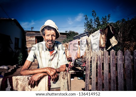 old african black man standing proudly in front of his home with washing on the line behind him