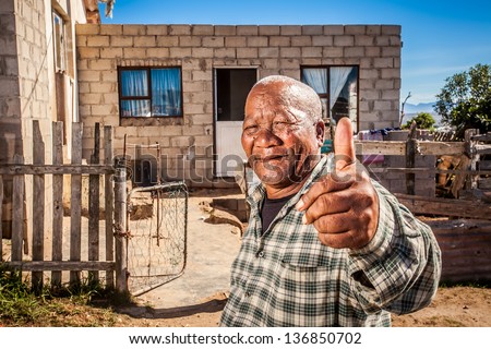 old african man showing thumbs-up in front of his house in the township