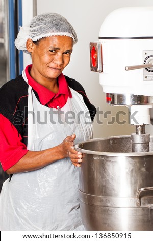 african colored baker mixing dough ingredients in an industrial electric mixer