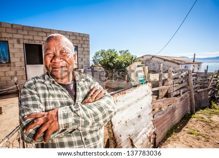 old african man standing proudly with his arms crossed in front of his home