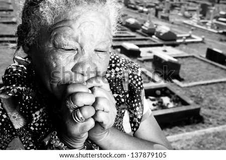 old homeless african woman sitting in front of the cemetery in prayer