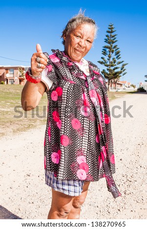 old homeless african lady standing in the dirt road showing thumbs up