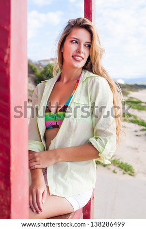 beautiful young caucasian woman with long hair sitting happily on the patio fence of a beach cabin