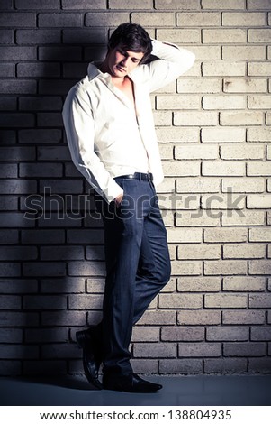 attractive young male model in formal wear leaning against a brick wall holding his neck