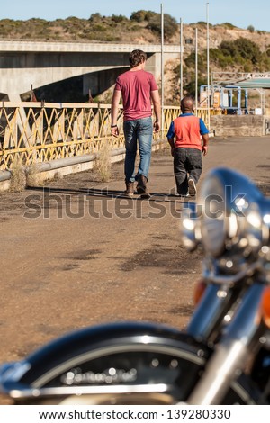 an young caucasian man walking along with his african dwarfish friend down the road
