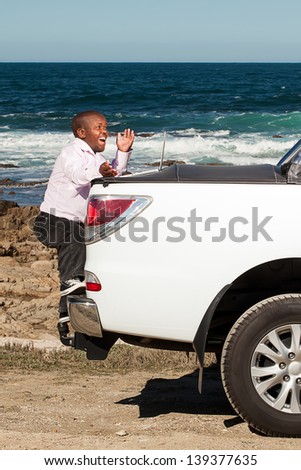 dwarfish african man stepping up on the back of a pickup truck with an expression of wonder while working on the laptop