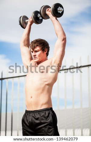 young caucasian man doing weight exercises outdoors dressed in black sweatpants
