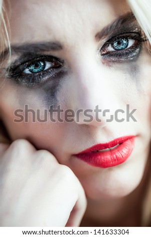 close-up portrait of a beautiful caucasian girl with dried up tears and black make-up smudged down her face resting her head on her fist