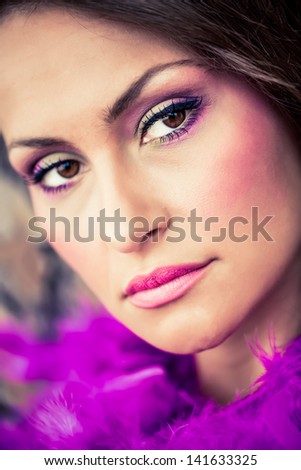 portrait of a beautiful brunette model with dark brown eyes wearing magenta make-up and covered in purple feathers