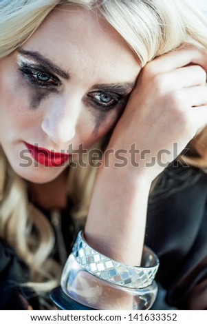 pretty caucasian model with blond hair wiping her teary smudged face with the back of her hand