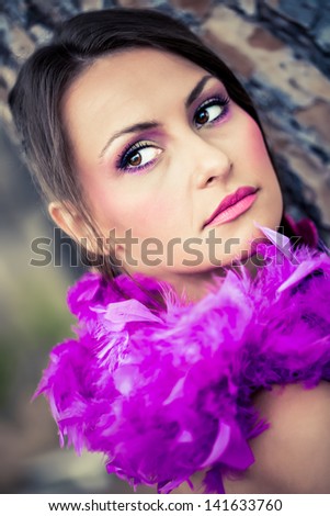 beautiful brunette model wearing magenta make-up with a purple feathered scarf leaning against a tree looking over her shoulder