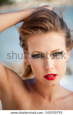 portrait of a beautiful young caucasian model wearing siren red lipstick holding her hair back with bare arms looking ravishing