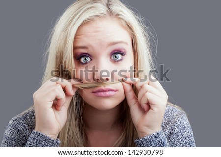 a pretty caucasian girl holding a piece of her long blond hair under her nose as a mustache and raising her eyebrows in silliness