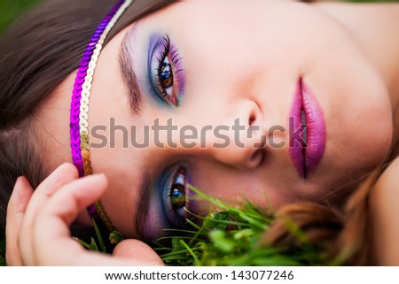 beautiful brunette model resting in the green grass of the park wearing a purple and gold headband with bright brown eyes staring back