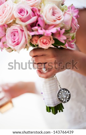 a cropped portrait of a brides hand holding her pink bouquet of roses with her engagement ring on her finger
