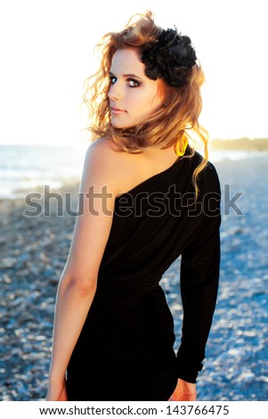 beautiful caucasian model with golden red hair looking over her shoulder while taking a walk on the rocky shore in the sunset
