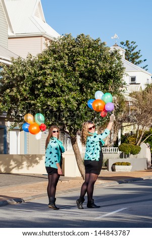 two pretty friend in matching clothing walking down a street holding balloons and looking back smiling