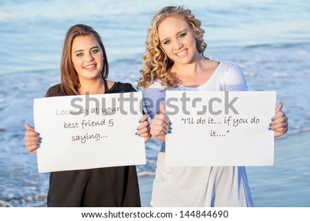 two pretty caucasian girls in contrast holding out a friendship quote smiling brightly with the ocean in the background